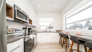 Une cuisine moderne avec des meubles blancs, des appareils en acier inoxydable et une grande fenêtre donnant sur l’extérieur.