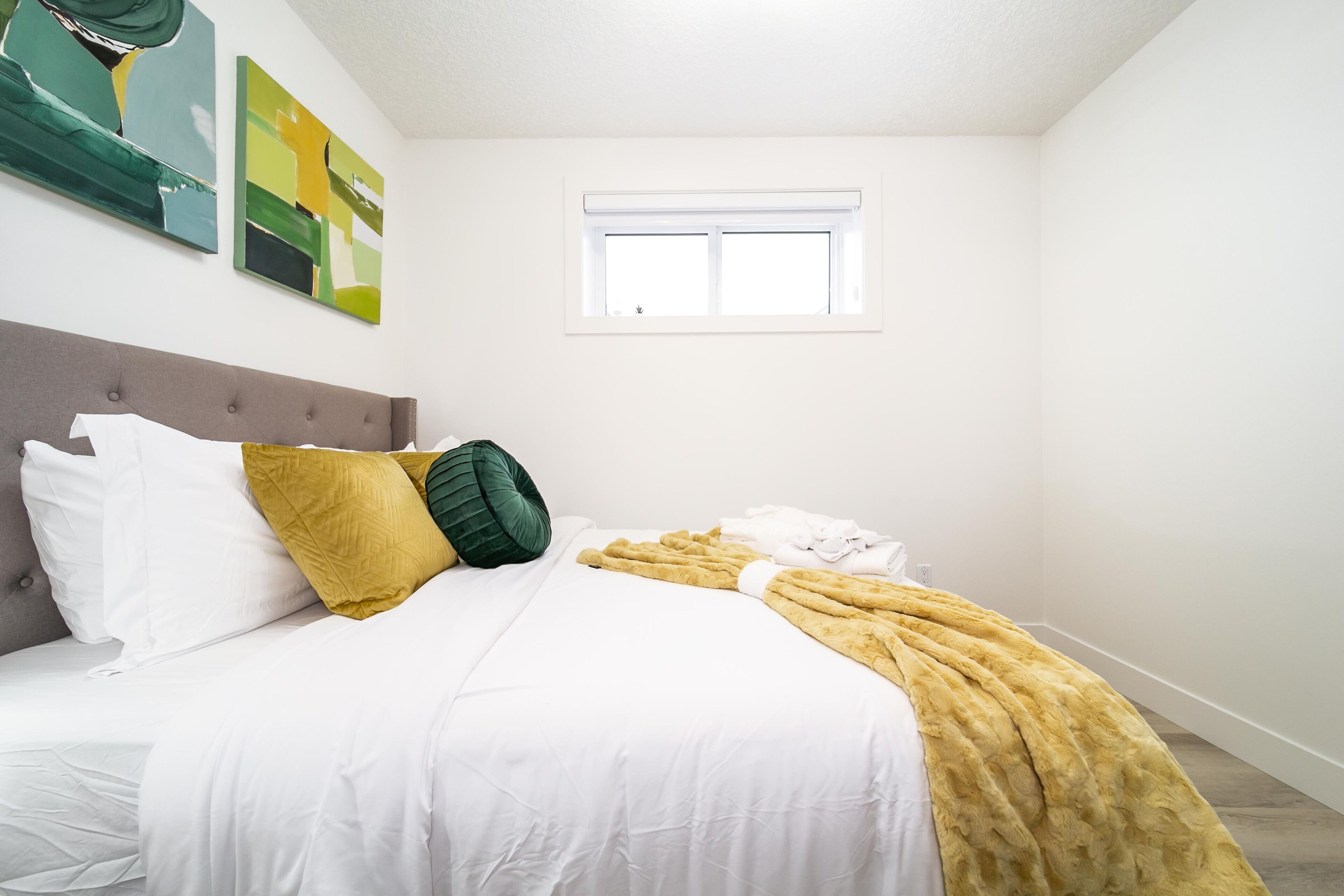 Une chambre à coucher avec un lit, du linge de lit blanc, une couverture jaune et un oreiller vert.