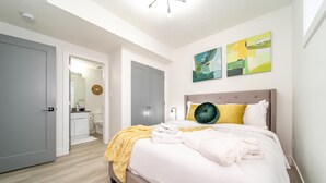 Une chambre à coucher avec un lit, une salle de bain visible à travers une porte ouverte et un luminaire au plafond.