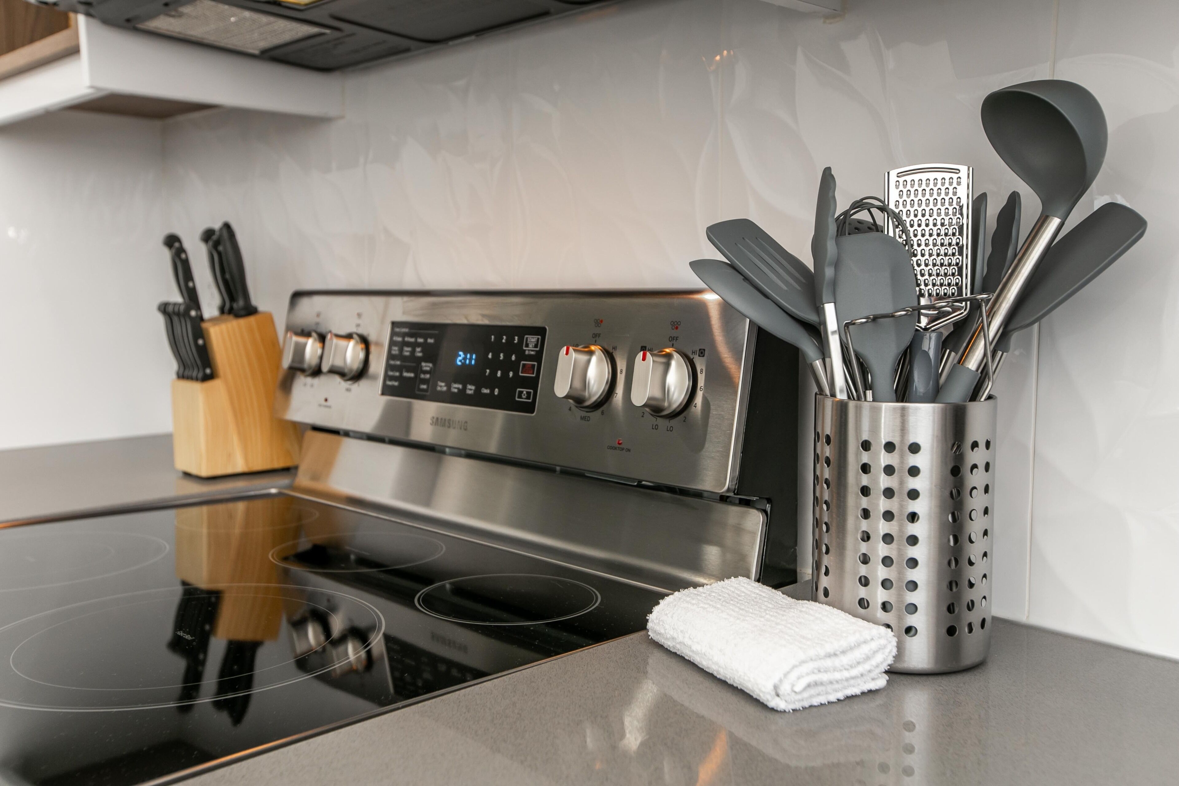 A modern kitchen with a stainless steel stove, a knife block, and a utensil holder.