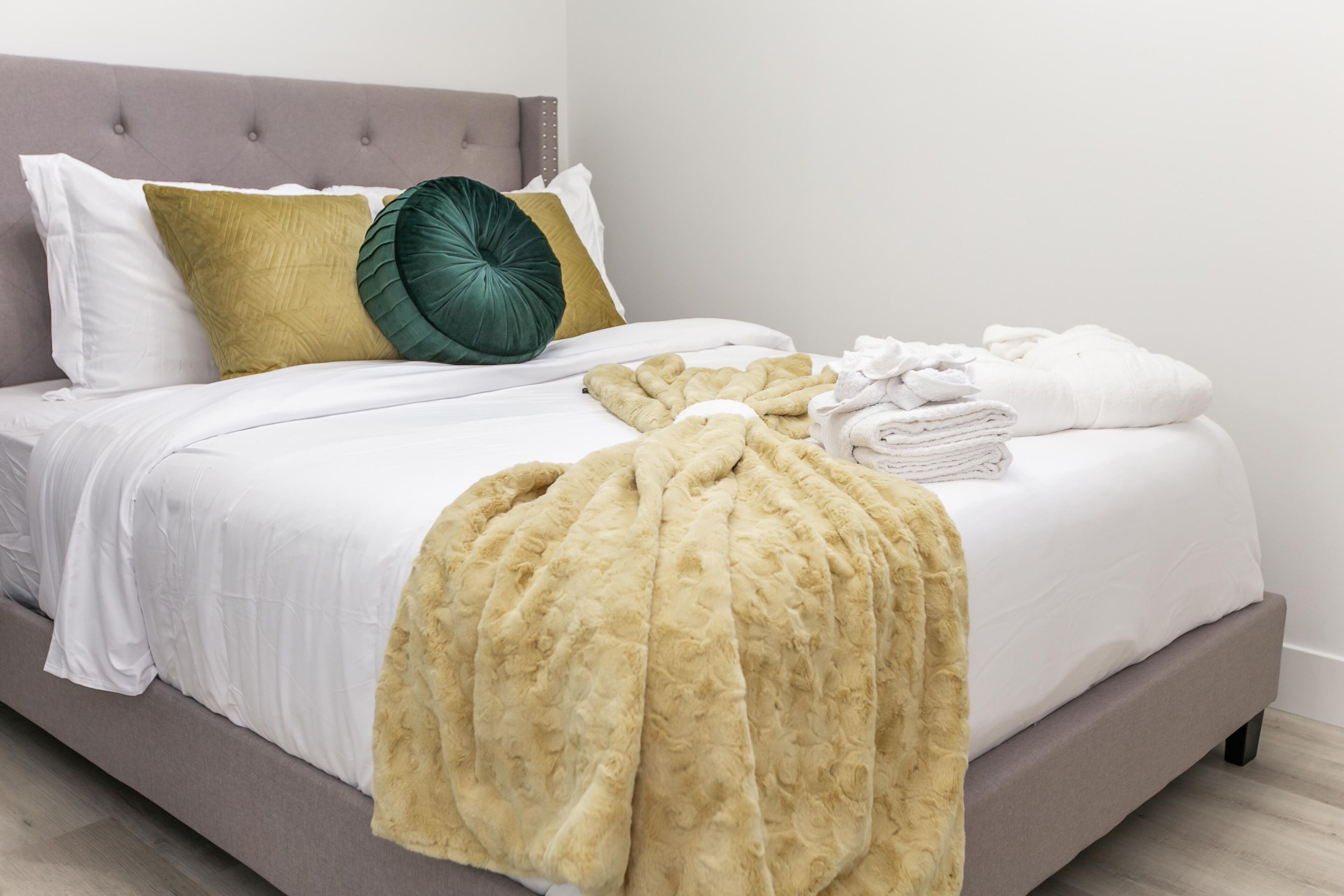 A neatly made bed with a beige blanket, a green pillow, and a folded white towel on the side.