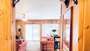 A wooden interior with a checkered sofa, a table with a red and white tablecloth, and a Christmas tree.