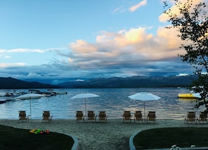 Relax by the serene lake with comfortable beach chairs and umbrellas, surrounded by majestic mountains.