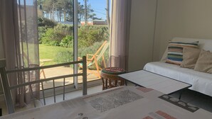 Een kamer met een bed, een klein tafeltje en uitzicht op een tuin door grote ramen.