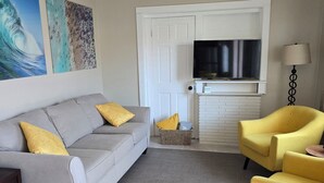 Una sala de estar con un sofá gris, cojines amarillos, un sillón amarillo, un televisor de pantalla plana y una lámpara.