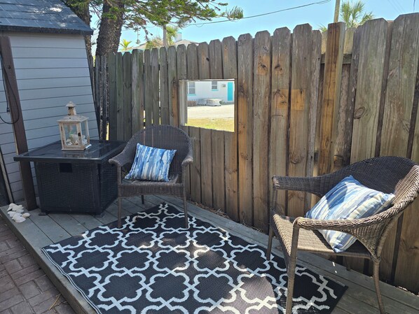 A patio area with two wicker chairs, a small table, and a patterned rug.