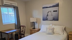 Un dormitorio ordenado con cama, escritorio, silla, lámpara y un cuadro en la pared.