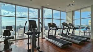 Ett gym med löpband, crosstrainers och motionscyklar, stora fönster med utsikt över palmer och stadens skyline.