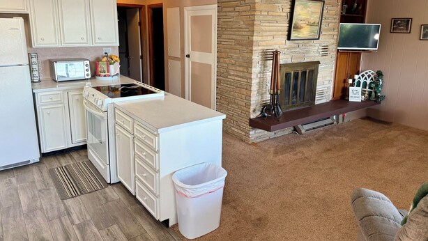 A compact kitchen with white cabinetry, a built-in oven, and a microwave. There's a stone fireplace with a mounted TV and a framed picture above it. - Relax and recharge at The Spot (Fall River)