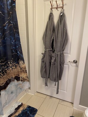 Bathroom features a shower, bathtub, and two bathrobes.
