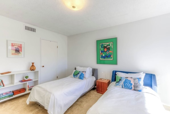 A bedroom with two beds, a bookshelf, a door, and a wall with a framed picture.