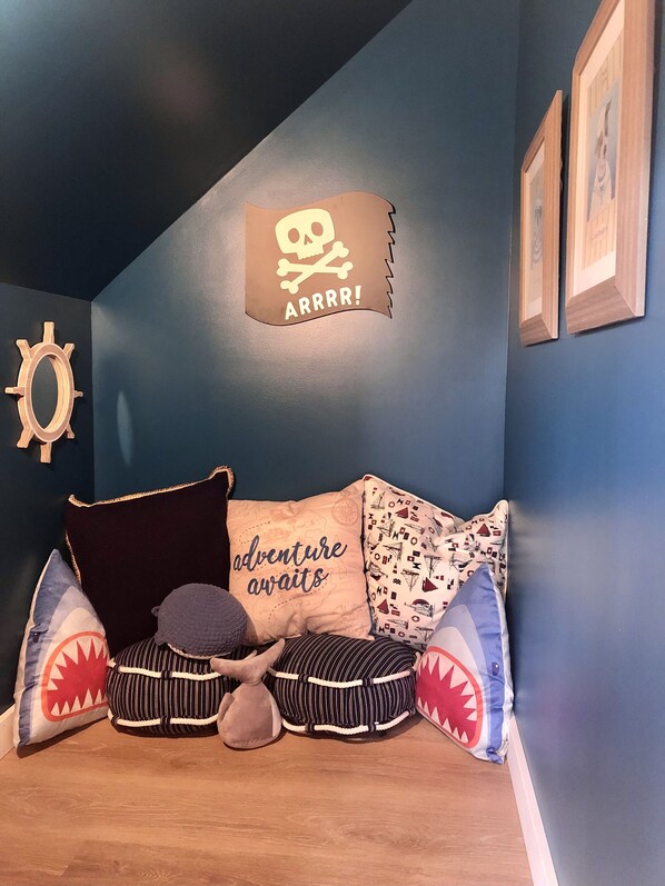 A cozy room with a blue wall, a wooden floor, a bed with striped pillows, and a skull and crossbones sign on the wall.