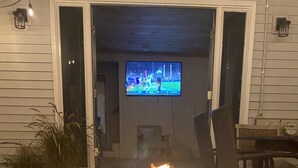 A circular outdoor fire pit with flames, surrounded by chairs and a television in the background. - Sea Breezy Vacation House, Unit 2 - 5 min WALK to beach!! (Old Orchard Beach)