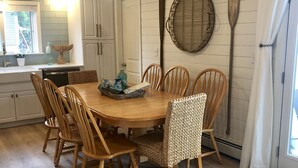 A wooden dining table surrounded by six chairs, a woven basket, and a hanging light fixture in a room with wooden paneling and a large window. - Sea Breezy Vacation House, Unit 2 - 5 min WALK to beach!! (Old Orchard Beach)