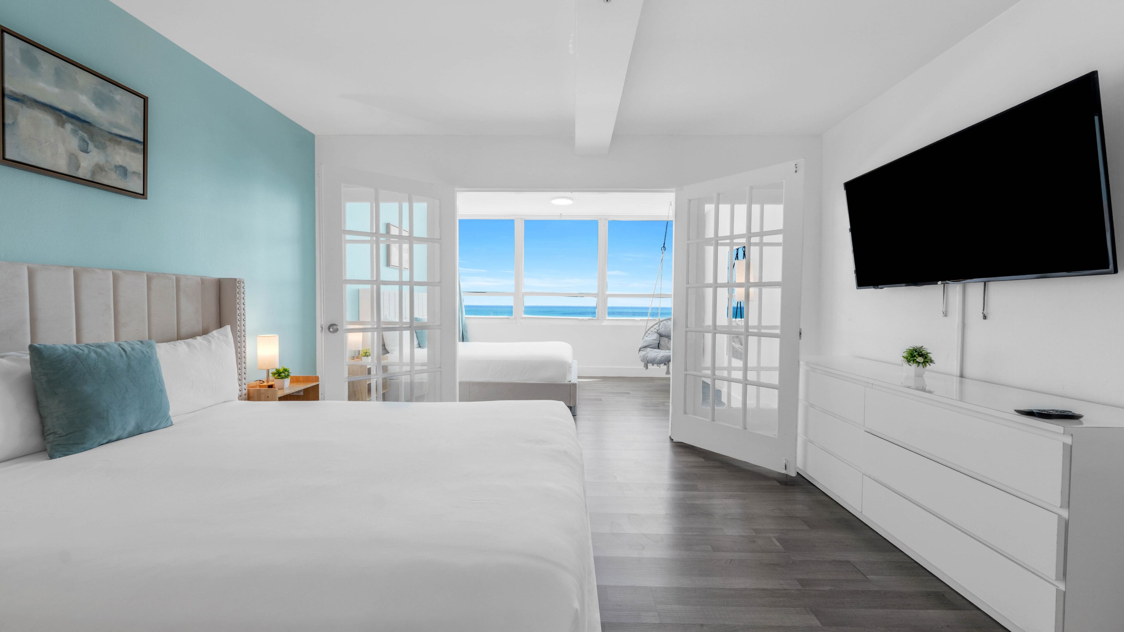 A modern bedroom with a large bed, a TV, and a view of the ocean.