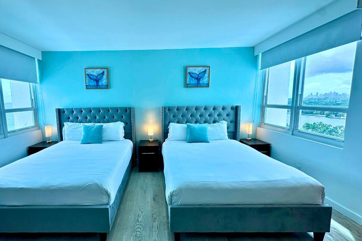 A twin bed room with a city view, two bedside tables with lamps, and artwork on the wall.