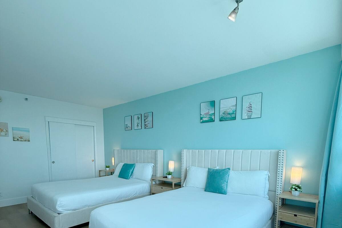 A bedroom with two beds, a door, and a wall with framed pictures.