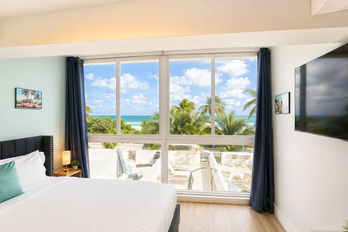 A bedroom with a large window, a bed, a nightstand, and a TV.