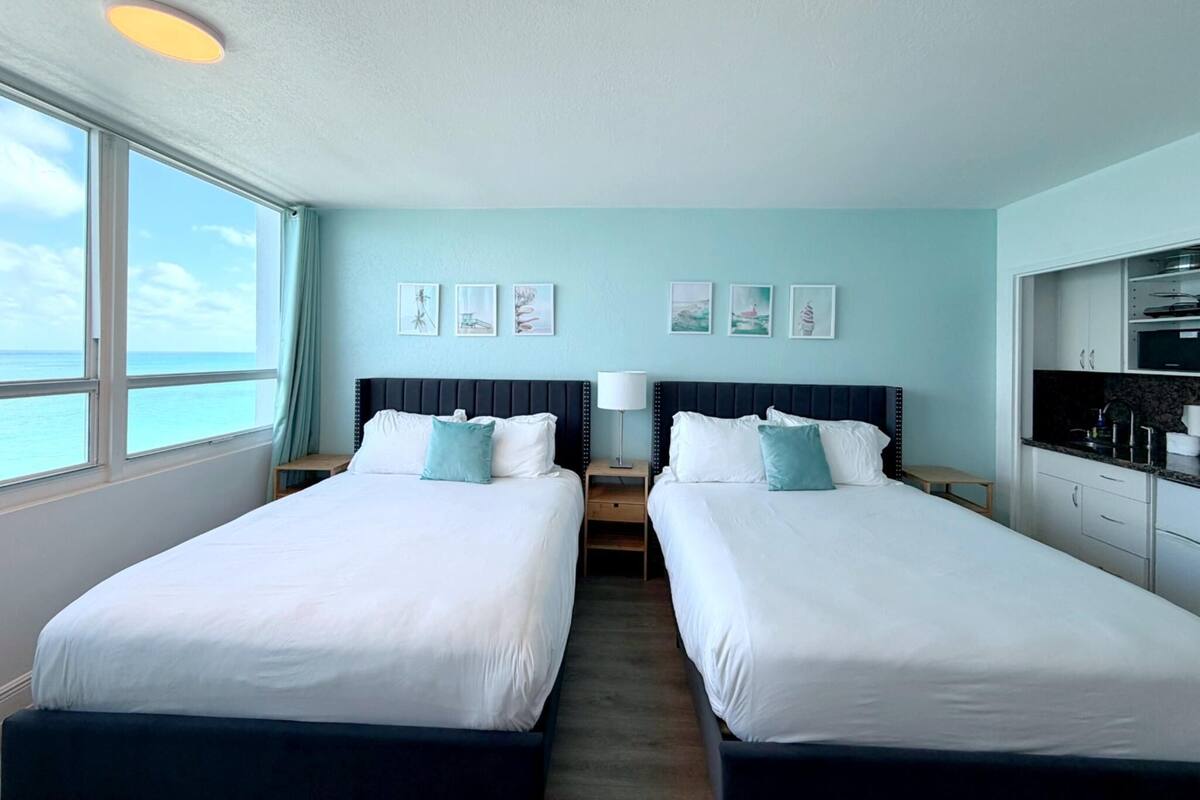 A hotel room with two beds, a view of the ocean, and a kitchenette.