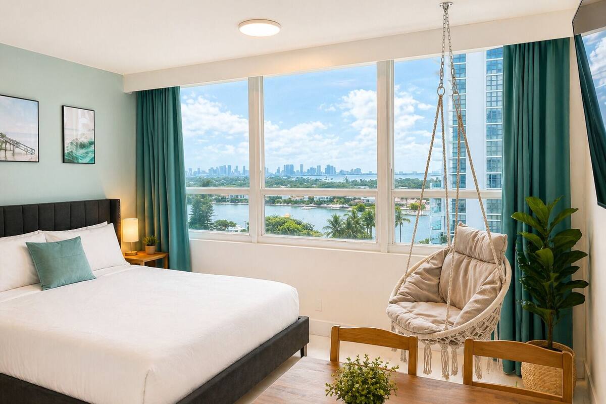 A bedroom with a bed, a hanging chair, a view of a cityscape, and a plant.