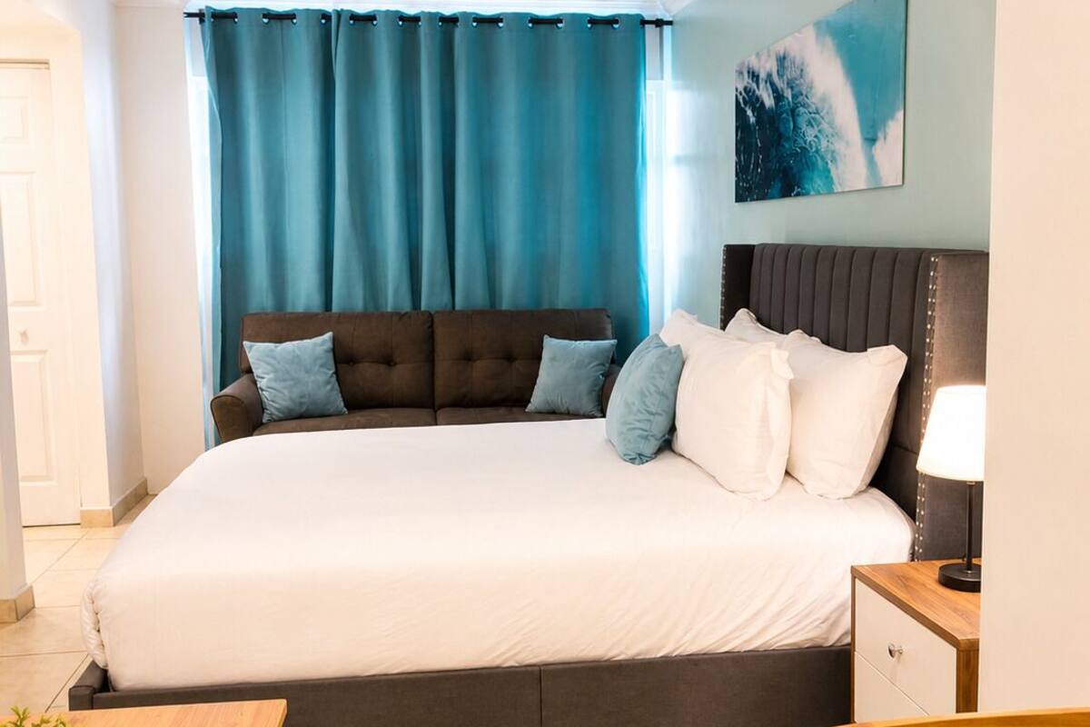 A modern bedroom with a large bed, a nightstand, a desk, and a potted plant.