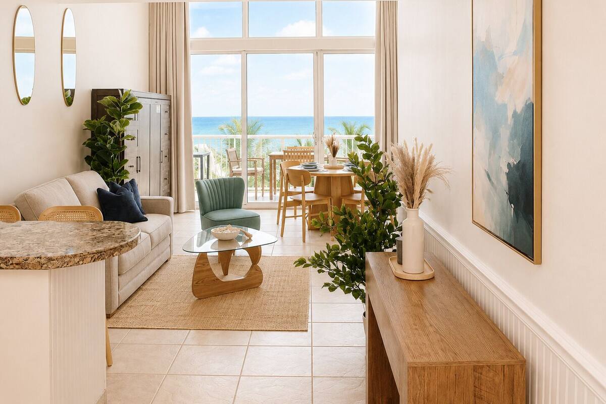 A modern living room with a view of the ocean, a dining area, and a large painting on the wall.