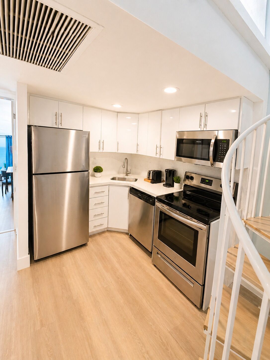A modern kitchen with stainless steel appliances, white cabinetry, and a wooden floor.