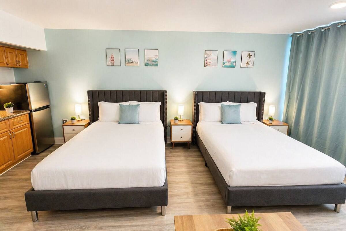 A hotel room with two beds, a kitchenette, and a view of the ocean.