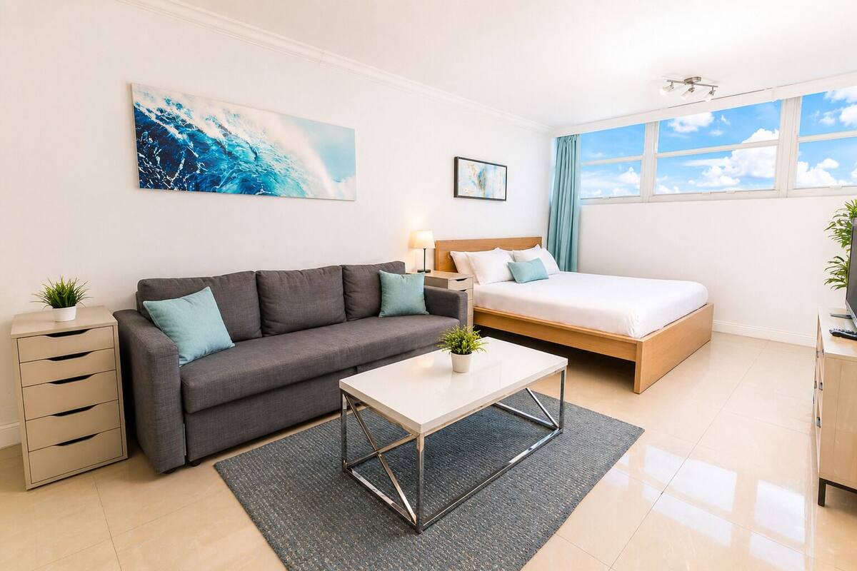 A modern room with a grey sofa, a bed, a small table, and a desk with a plant.
