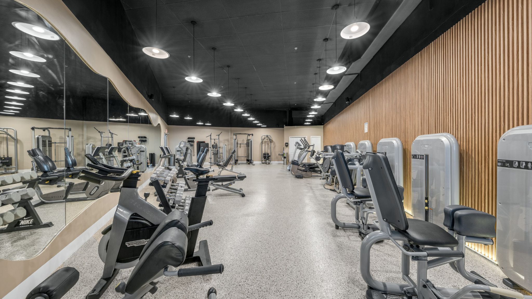 A gym with various exercise machines, mirrors, and a wooden wall.