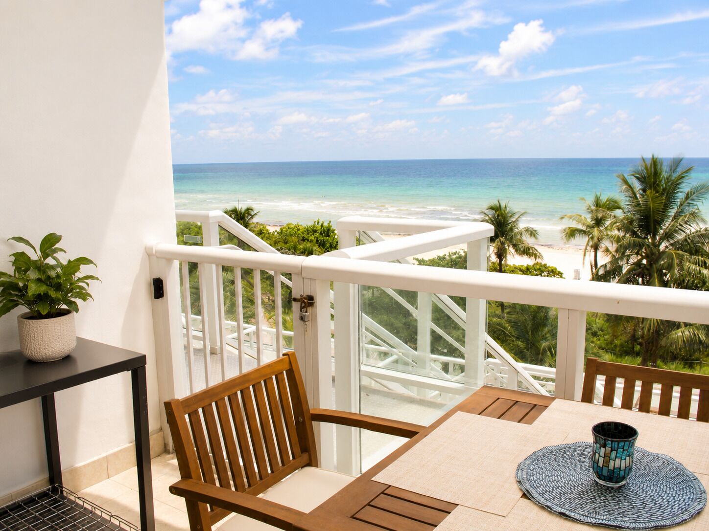 Un balcon avec vue sur la plage, une table avec des chaises et une plante en pot.