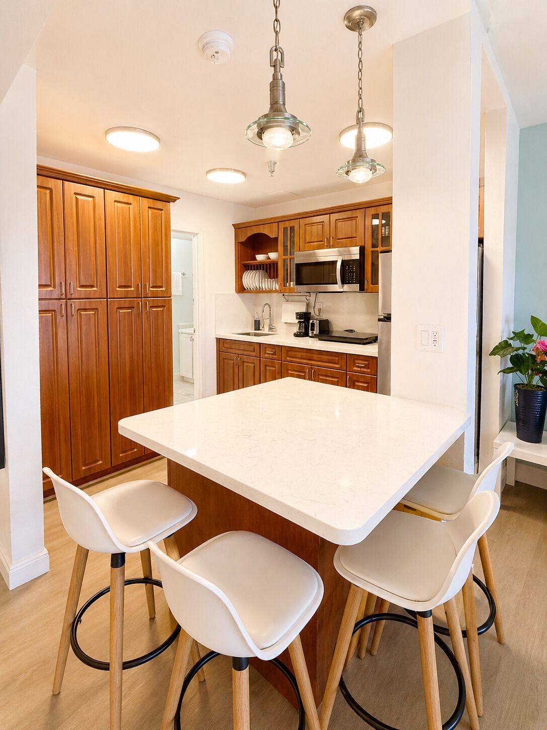 A modern kitchen with wooden cabinets, a large island with bar stools, stainless steel appliances, and pendant lighting.