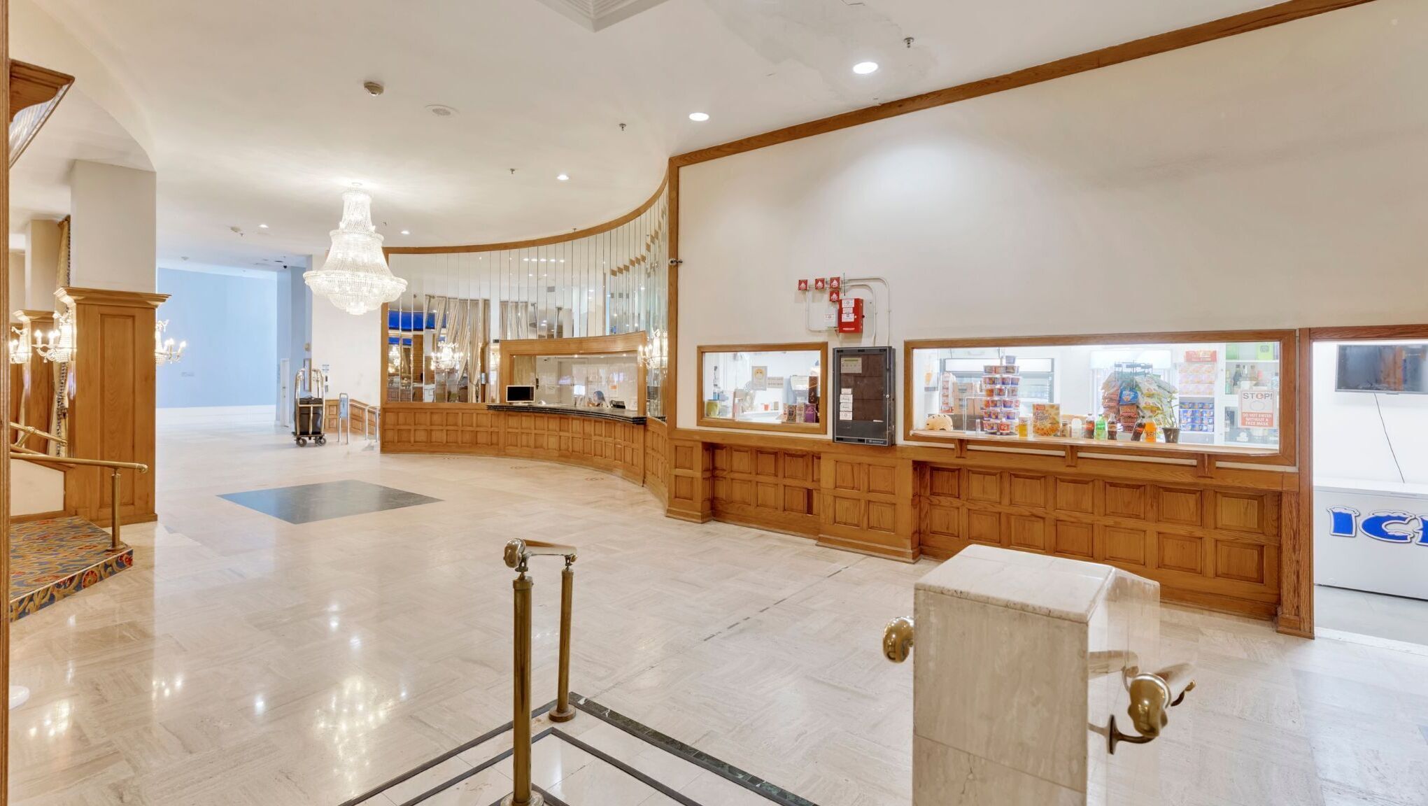 A hotel lobby with a curved reception desk, a chandelier, and a view of the street outside.