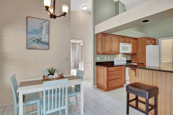 A modern kitchen with wooden cabinets, a microwave, and a refrigerator. There is a dining area with a table and chairs, and a painting on the wall. - SUPERB LAKESIDE VILLA WITH PRIVATE POOL NAPLES (Naples)