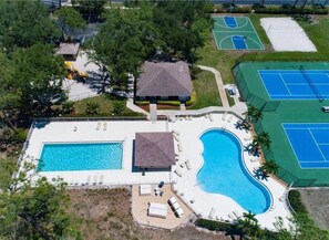 Luftaufnahme eines Resorts mit großem Schwimmbad, Tennisplätzen und einem kleinen Gebäude.
