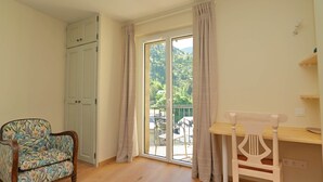 A room with a wooden floor, a desk with a chair, a patterned armchair, a sliding glass door, and a white wardrobe. - Montserrat Figueras - 4 en-suite bedrooms - Gite 8 people (Llo)