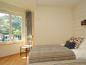 Un dormitorio con un ventanal grande, una cama con ropa de cama a rayas, una silla y un cabecero de madera.