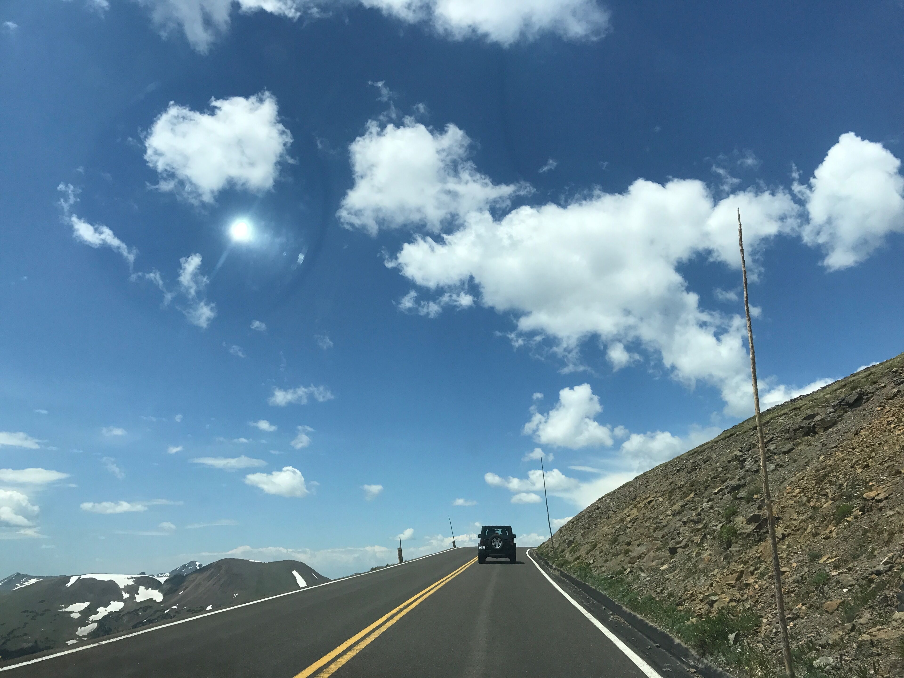 Una carretera con un vehículo, cielo despejado y montañas al fondo.