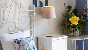 A neatly made bed with a floral pillow, a bedside table with a lamp, and a small table with a vase of flowers. - 5m walk to sandy beach, restaurants & shops! (Rethymno)