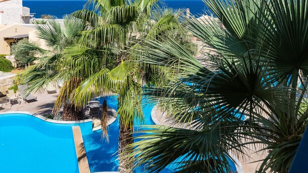A pool area with palm trees and a view of the ocean. - 5m walk to sandy beach, restaurants & shops! (Rethymno)