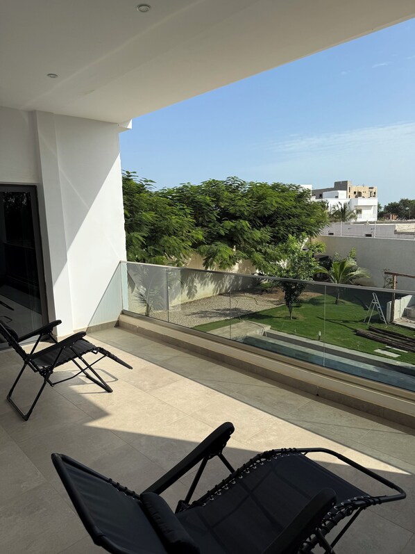 Un balcon avec deux fauteuils noirs, une vue dégagée sur une pelouse verdoyante et des arbres, et un bâtiment blanc en arrière-plan.