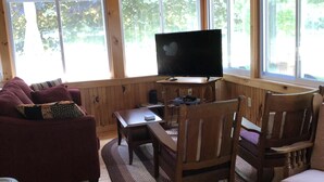 A wooden-paneled room with a television on a wooden table, a sofa, and two chairs. - Spacious Cottage with Lake Access in quiet lakeside community (Georgia)