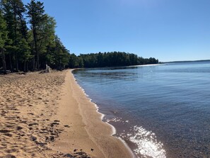 Ein Strand mit klarem Wasser, sandigem Ufer und bewaldeter Kulisse.