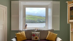 A room with a view of a river and hills, a sofa with cushions, and a window with shutters. - Traditional cottage with stunning views and walks on the doorstep. (Holmbridge)