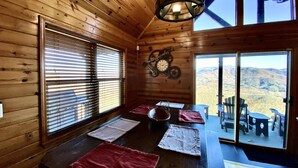 Interior de una cabaña de madera con comedor, ventanas amplias y vistas a la montaña.