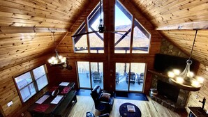 Amplia habitación tipo loft con techos altos y ventanas grandes, con chimenea, zona de estar y vistas al exterior.