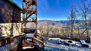 Una estructura de torre de madera con una escalera, un muro de piedra y vistas a montañas.