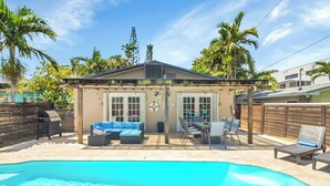 Ein Garten mit Swimmingpool, einer überdachten Terrasse mit Sitzgelegenheit und einem Grillbereich.