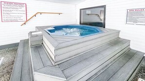 Ein Whirlpool mit Holzterrasse und Stufen, umgeben von weißen Wänden.