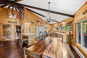 A spacious wooden cabin with a large dining table, kitchen area, and a chandelier. - Beary Round Retreat - Views, 3 Master Suites, Minutes to Downtown, Large Deck! (Maggie Valley)